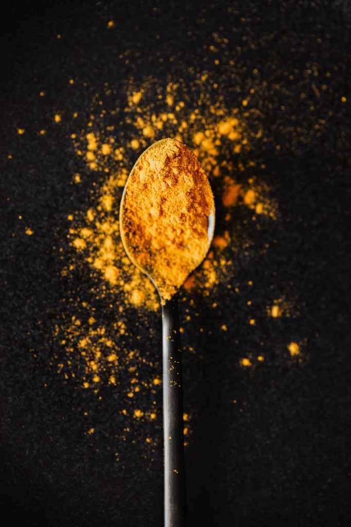curcuma powder on tablespoon and spilled on black surface