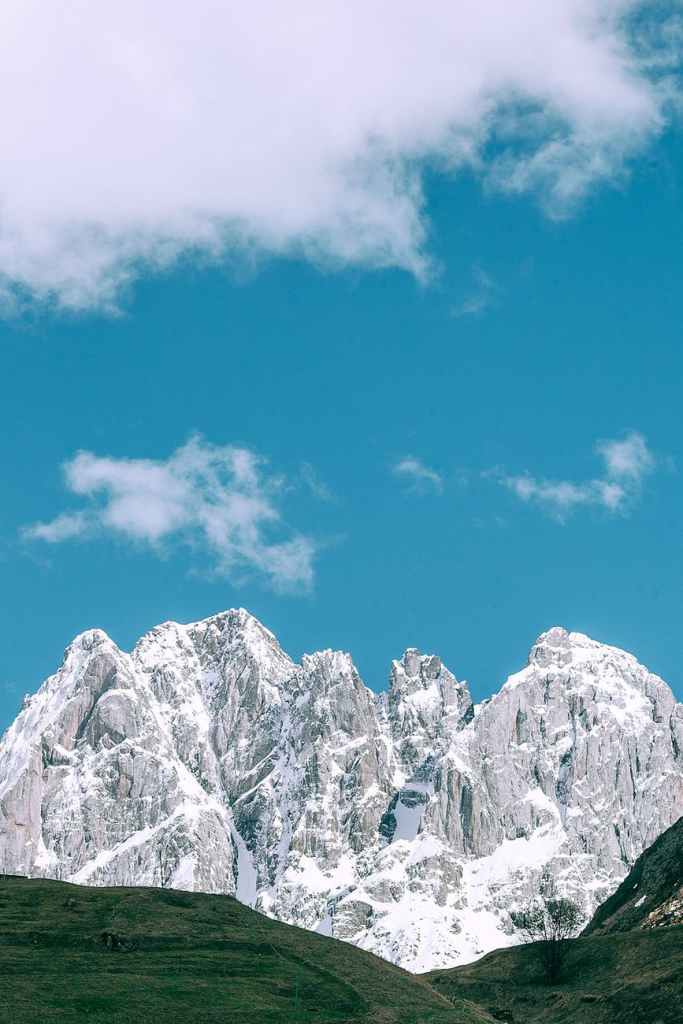 mountains peaks covered with snow behind green hills on partly cloudy day
